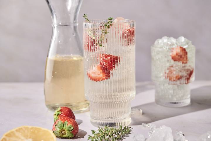 Classic White Wine Spritzer A tall glass of white wine spritzer garnished with strawberries and thyme sits next to a carafe of wine.