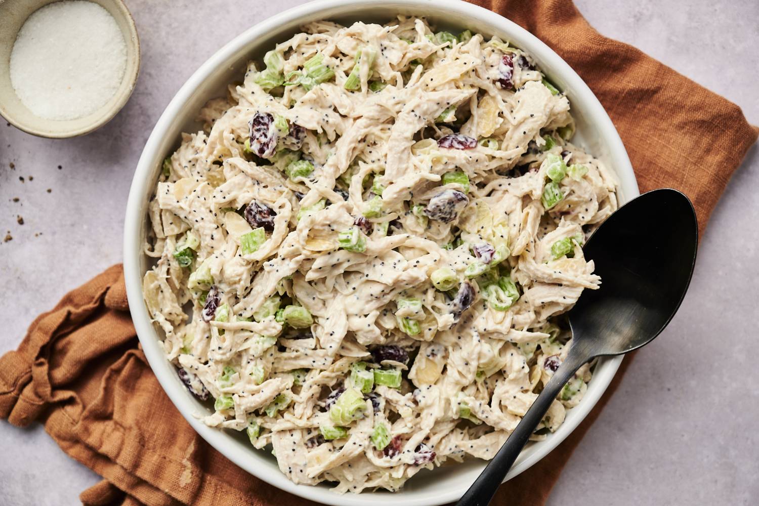 A bowl of cranberry almond chicken salad, garnished with a sprig of rosemary.