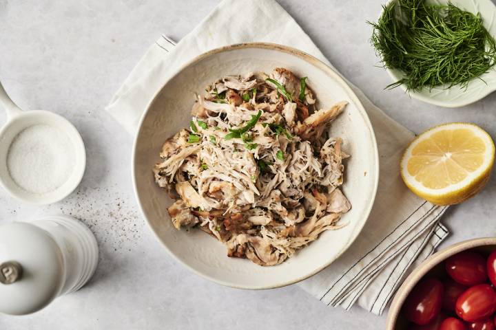 Easy Greek Chicken (Instant Pot, Slow Cooker, or Stovetop) A bowl of shredded Greek chicken, garnished with fresh herbs. Surrounded by lemon, dill, cherry tomatoes, and salt, creating a fresh Mediterranean feel.