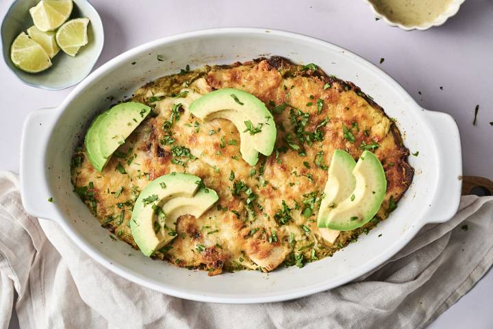 A freshly baked dish of enchiladas topped with avocado slices, sour cream, cilantro, and seasoning.