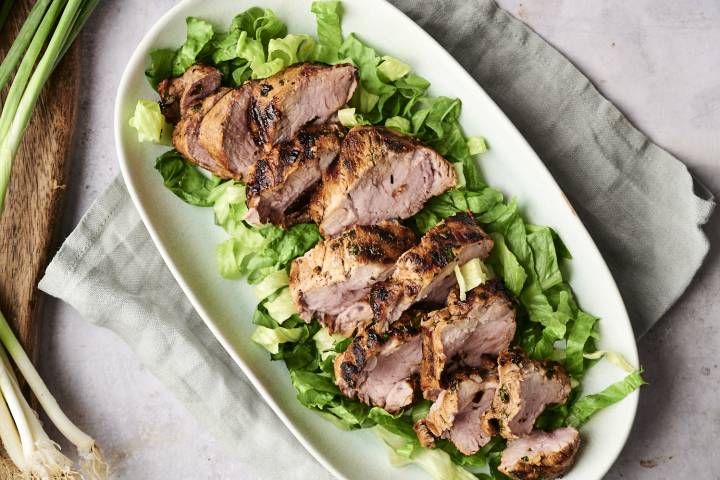 Sliced grilled pork tenderloin arranged on a bed of crisp chopped lettuce.