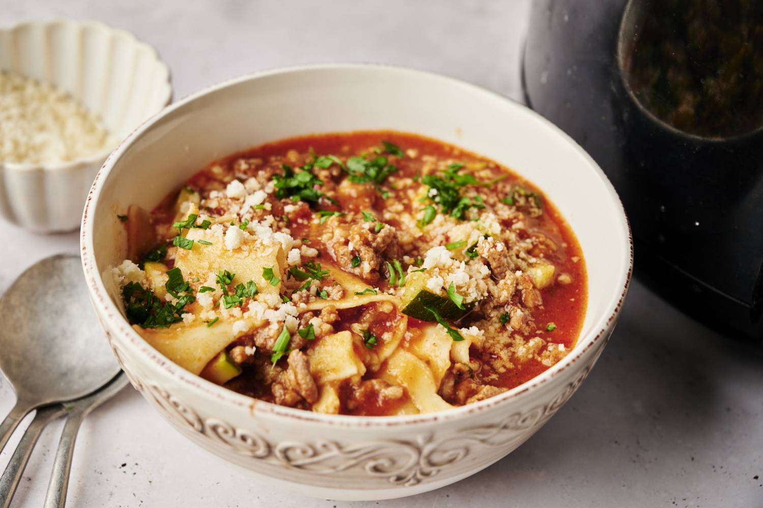 A bowl of lasagna soup with a rich tomato broth, ground meat, zucchini, and lasagna noodles, topped with parmesan cheese and fresh parsley.