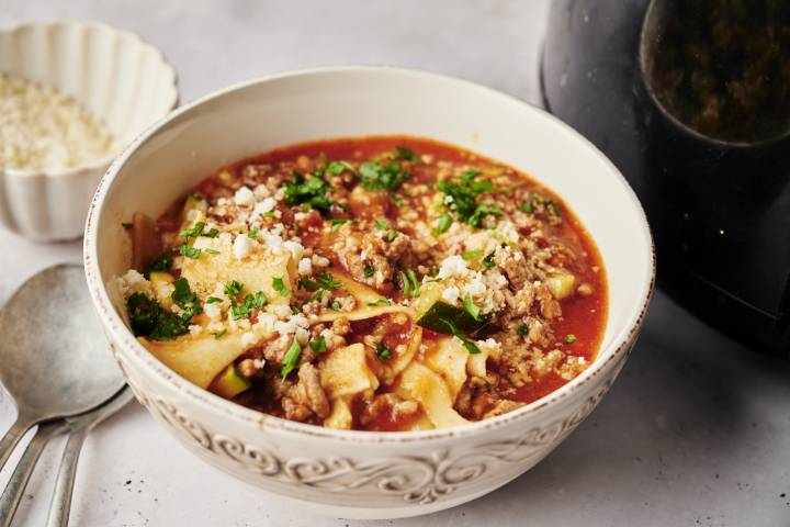 Healthy Slow Cooker Lasagna Soup A bowl of lasagna soup with a rich tomato broth, ground meat, zucchini, and lasagna noodles, topped with parmesan cheese and fresh parsley.