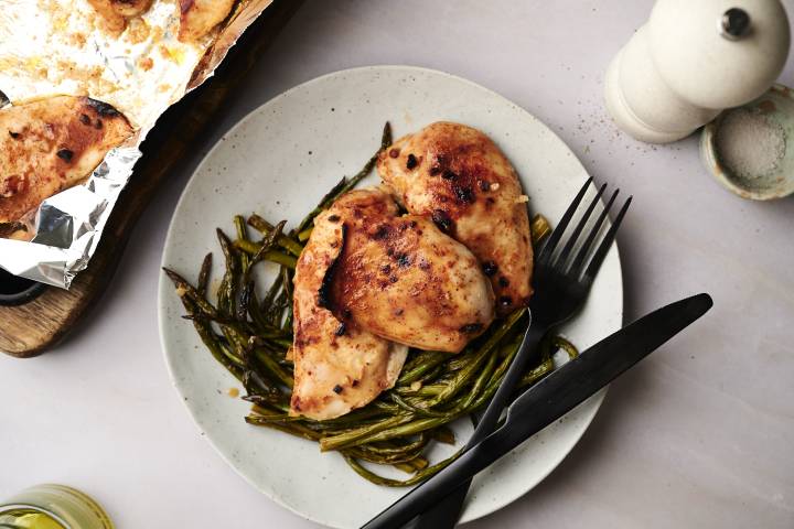 A plate of cooked honey garlic chicken and asparagus, garnished with sesame seeds and fresh parsley.