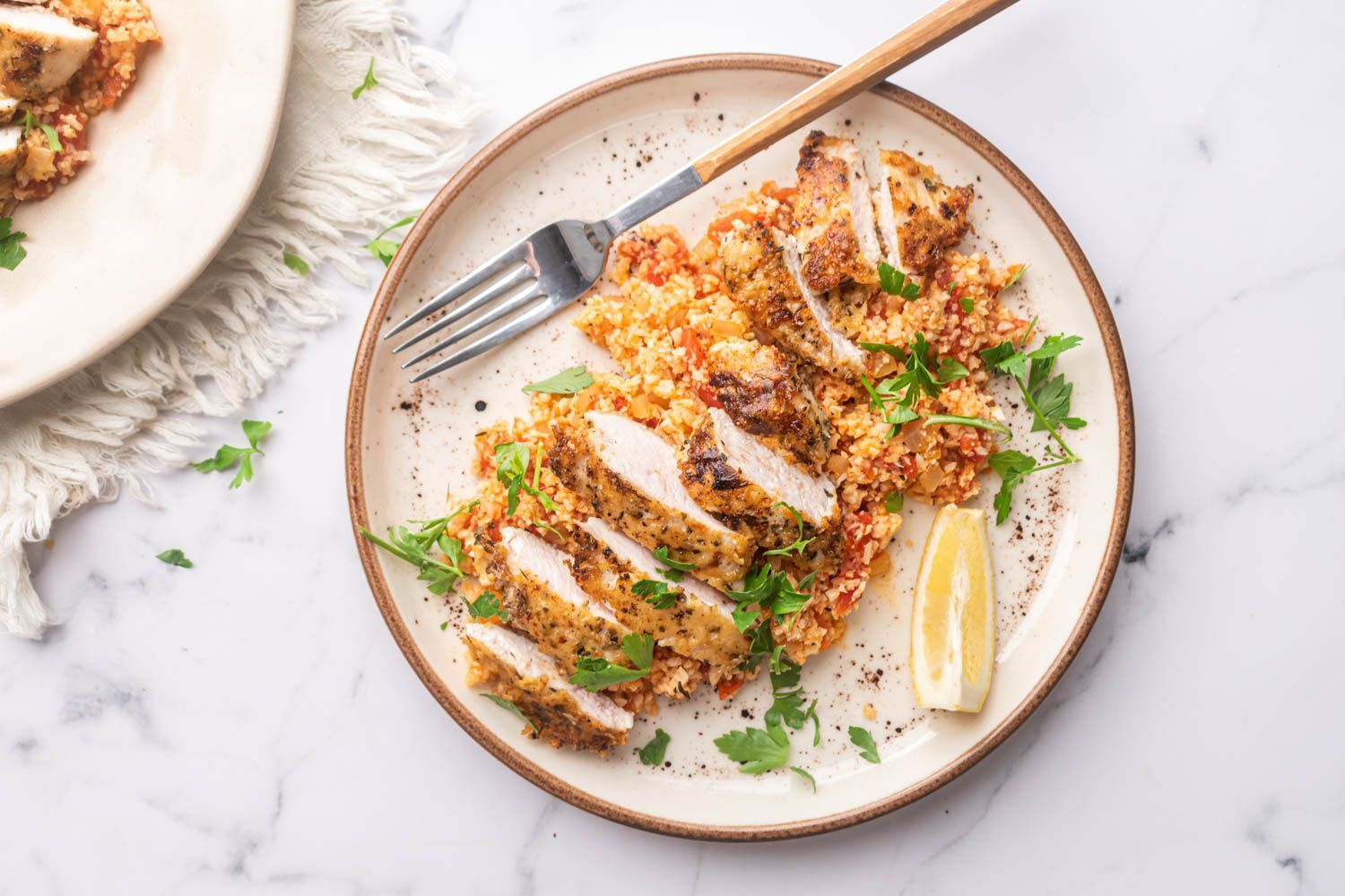 Garlic Parmesan Chicken and Cauliflower Rice Garlic parmesan chicken breast and cauliflower rice on a plate with fresh parsley and lemon.