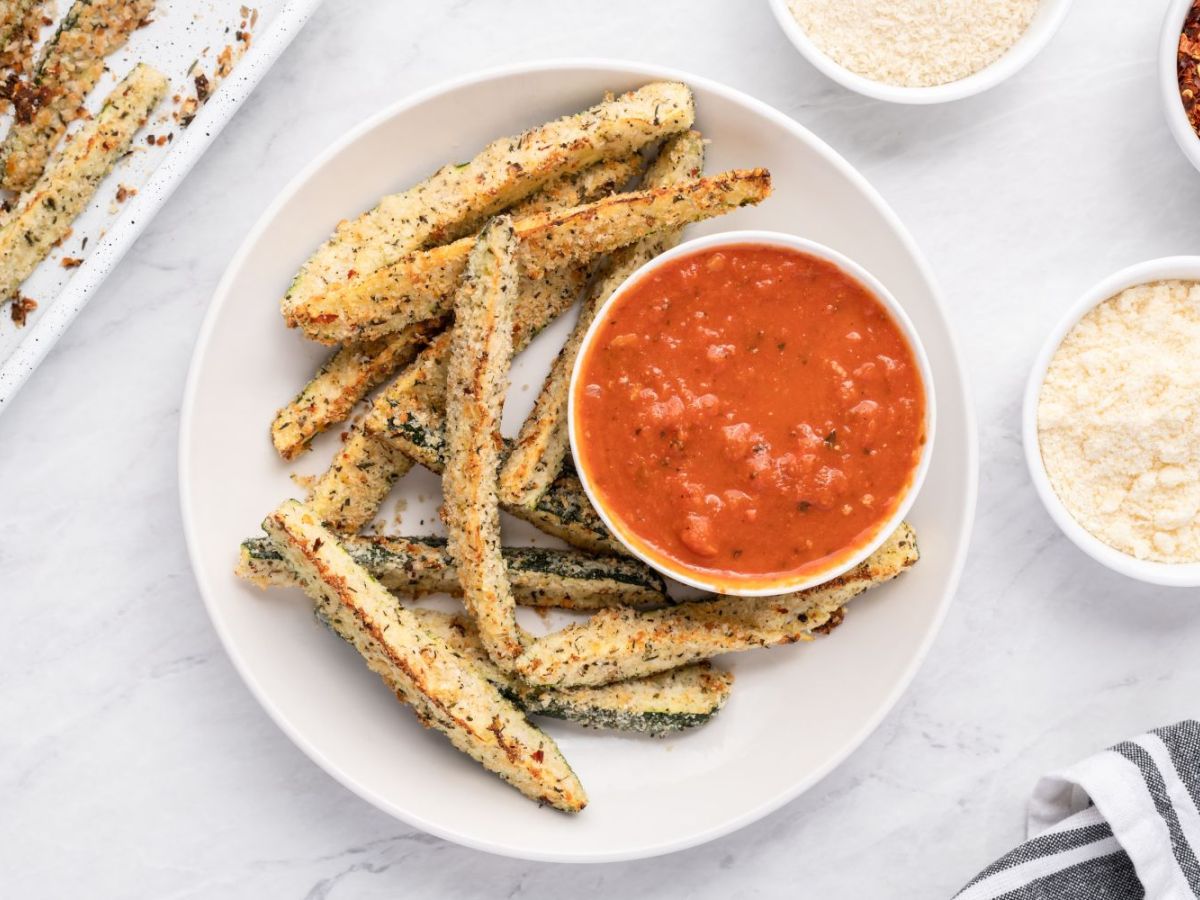 Vegetable Side Dishes Baked Parmesan zucchini fries with a crispy panko breading on a white plate with marinara sauce.