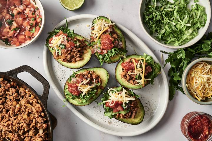 Mexican-style stuffed avocados on a white plate, filled with fresh ingredients and garnished with lime and cilantro.